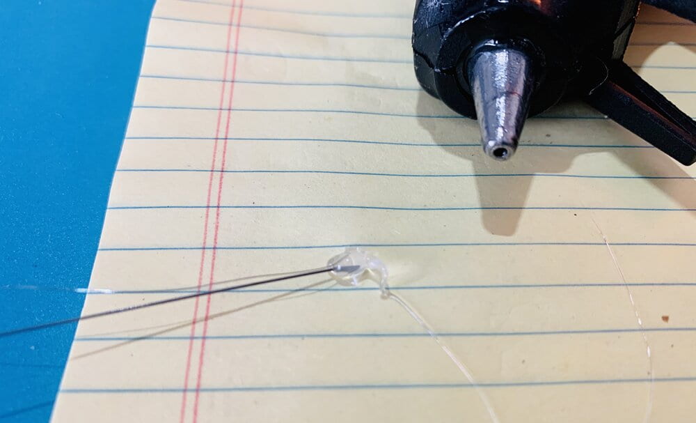 glue gun resting on a piece of paper with hot glue on the end of a wire